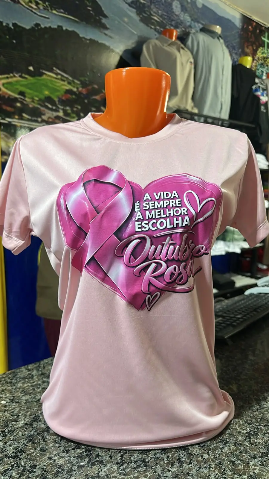 Camiseta rosa-clara com laço e arte de Outubro Rosa, fotografada em manequim na loja